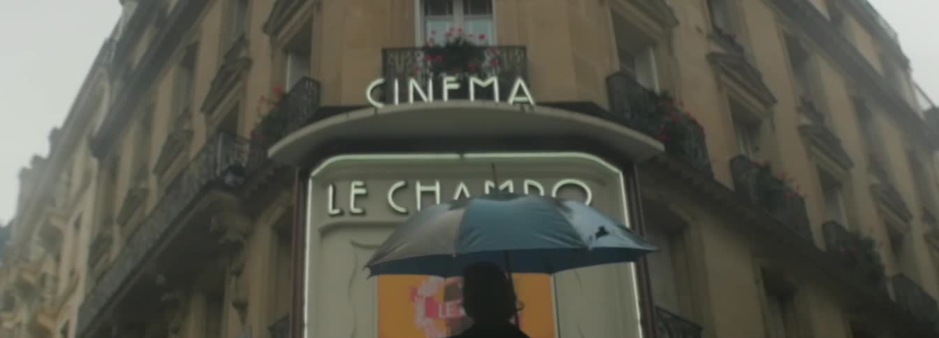 A woman carrying an umbrella approaching a cinema