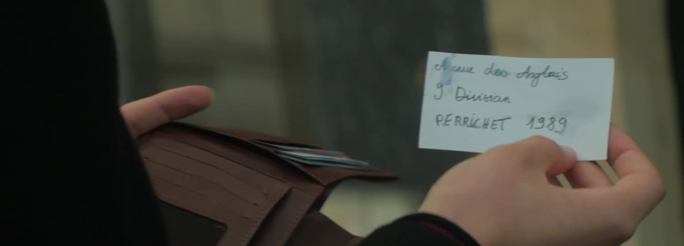 A person holding a wallet flips a business card over in their hand to show handwritten information