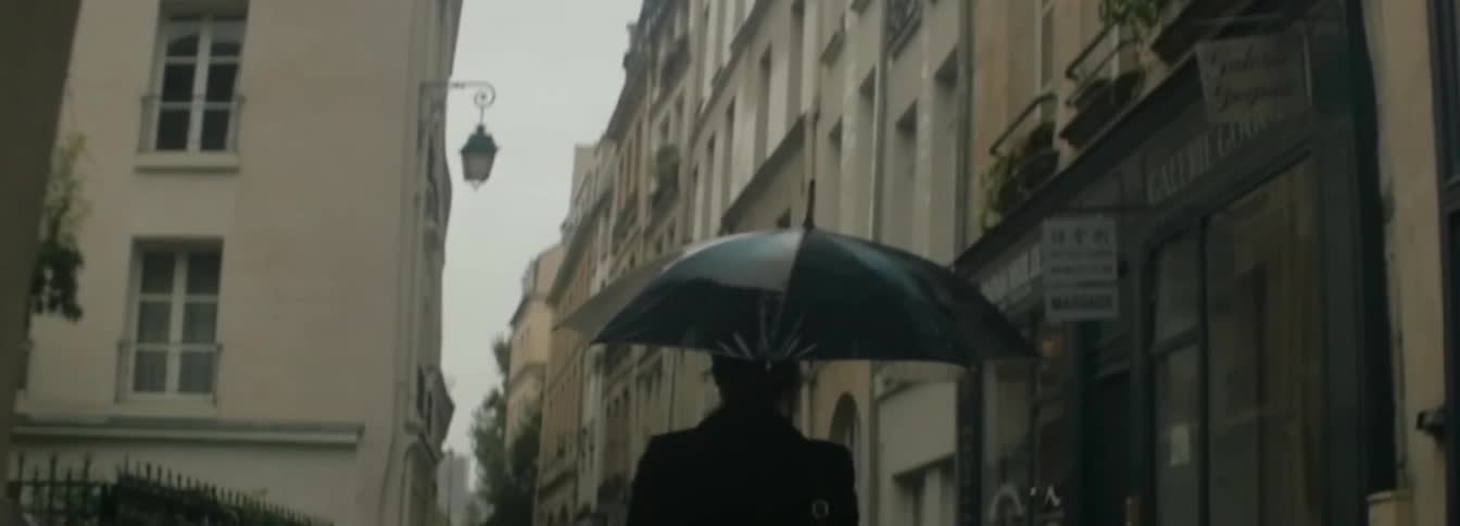 A woman holding an umbrella walking down a narrow street in a city on a rainy day