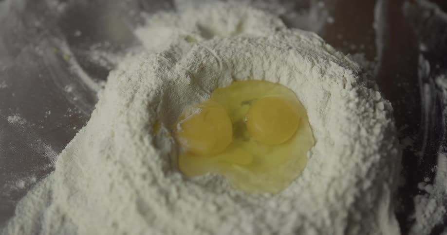 A man adds eggs to a pile of flour on the counter to make a dough