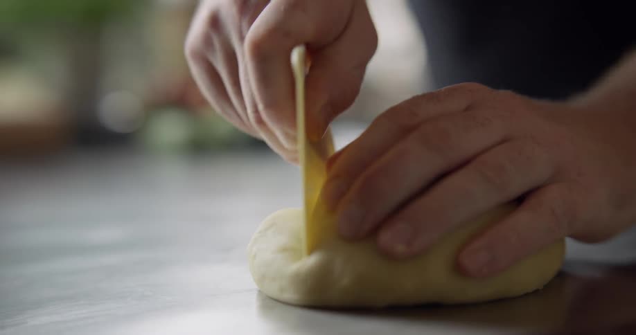 A chef trims a dough ball on a prep table