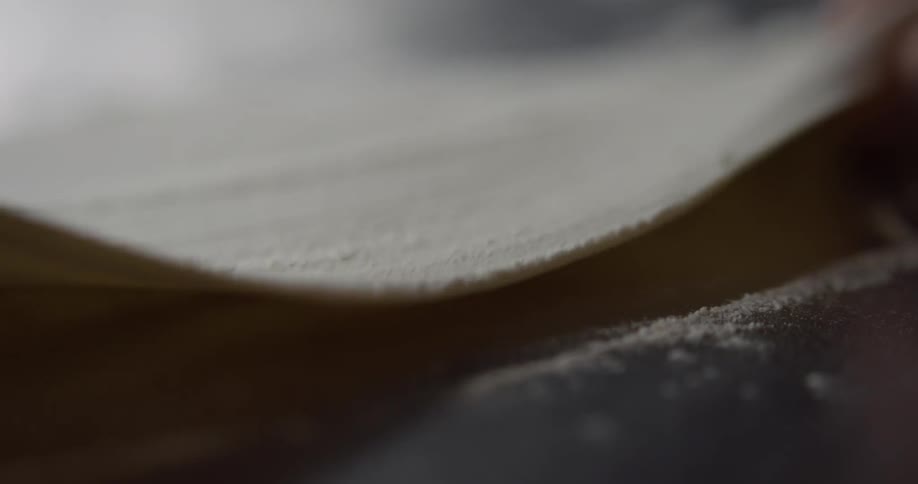 Flour is being spread across a thin layer of dough and flipped over