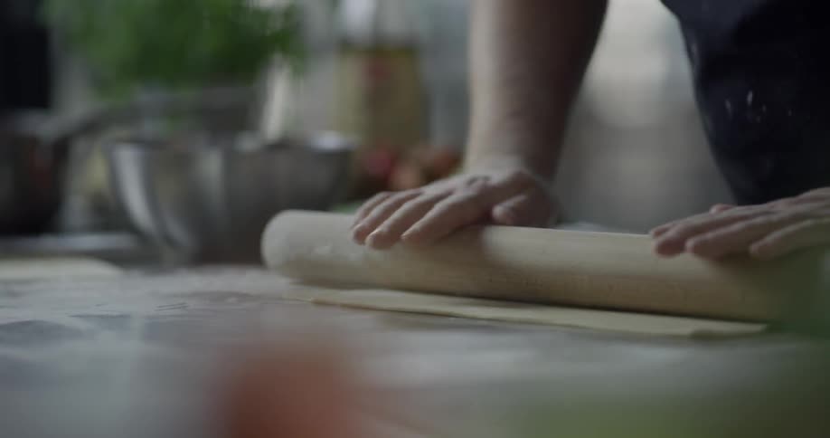 A man flattening pasta with a wooden roller