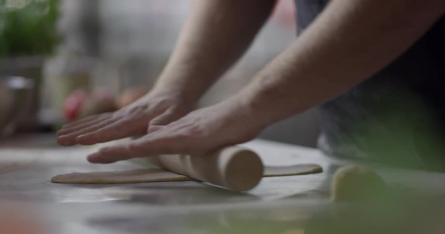 Baker rolling out dough with a large wood roller on the counter