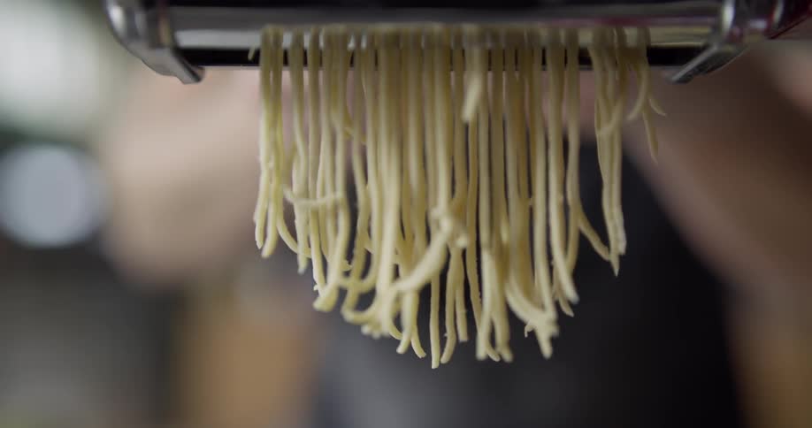 Handmade spaghetti comes out of a roller