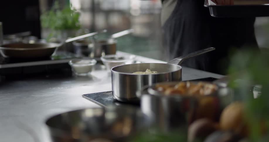A man with an apron taking noodles out of a tray and putting it in a pot