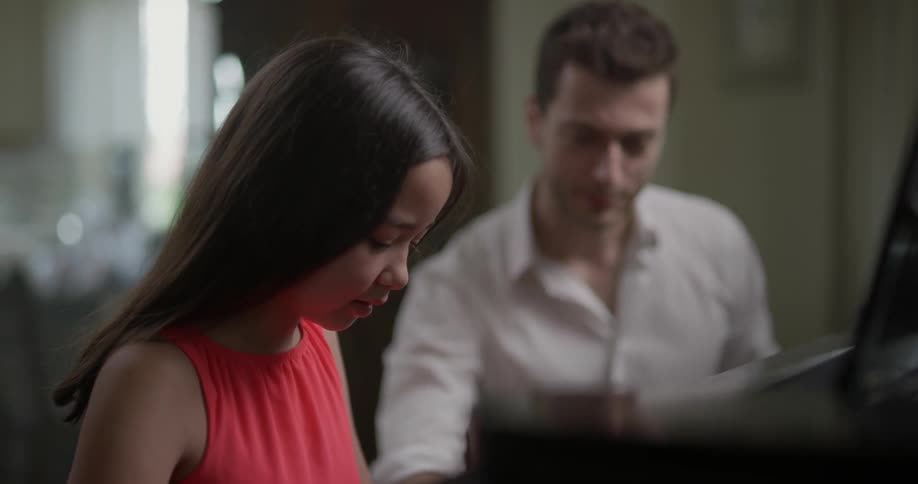 A young girl laughs while playing a piano with an instructor