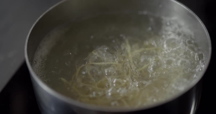 Spaghetti is being put into the boiling water on the stove in the kitchen