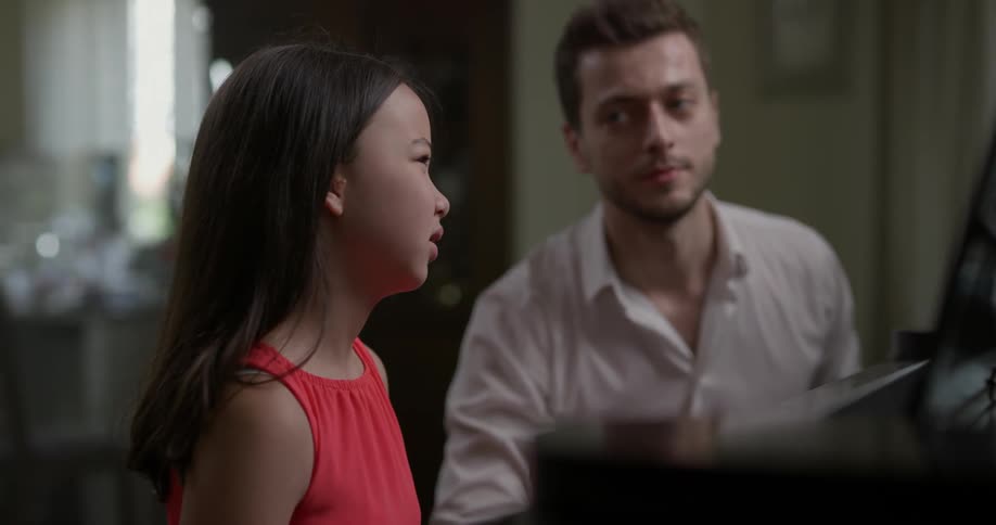 Man wearing white shirt teaches girl the musical notation indoors during daylight