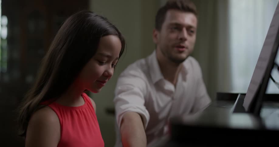 A girl learning to play piano from a older man
