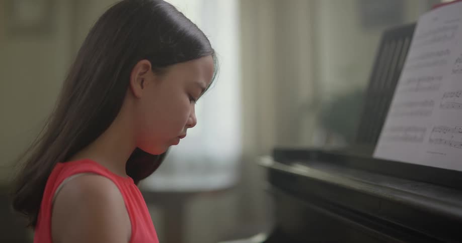 A young female sits at a piano an concentrates on the keys as she plays a song