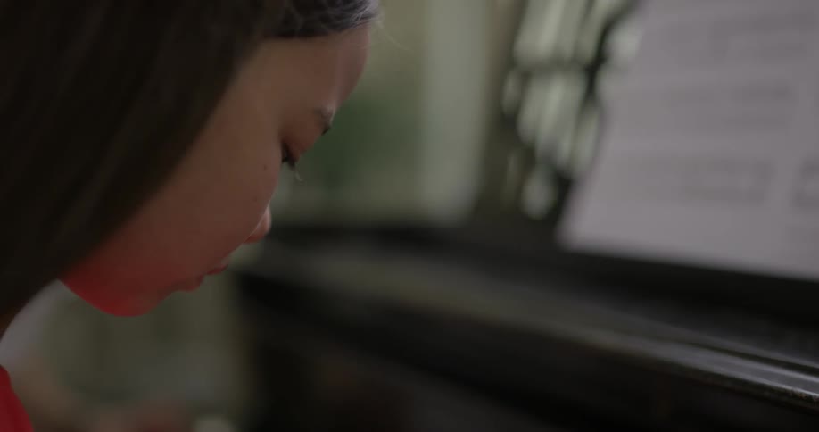 A young woman looks at the keys as she plays the piano