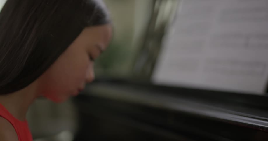 Asian girl who wears red dress play the piano indoors during daylight