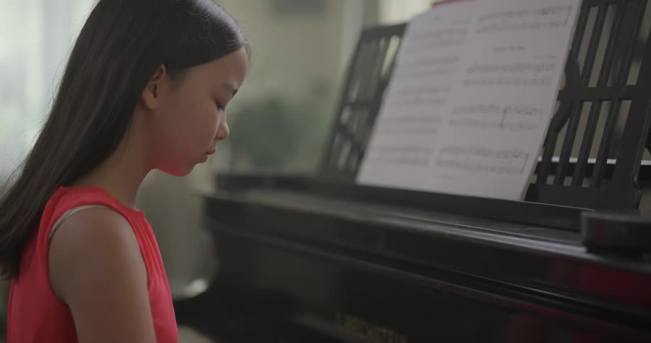 A young girl playing a piano in a soft red dress