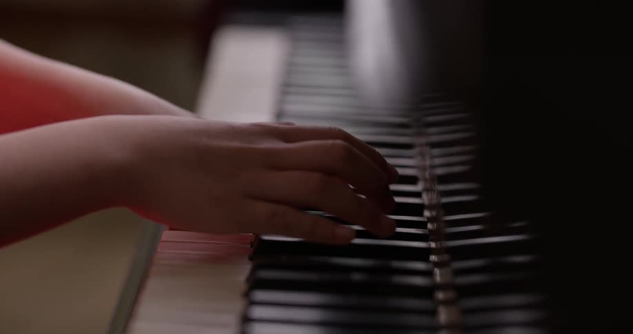 A child in a salmon pink dress plays the piano with both hands