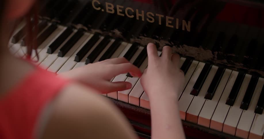 Girl wearing red dress play the piano indoors during daylight