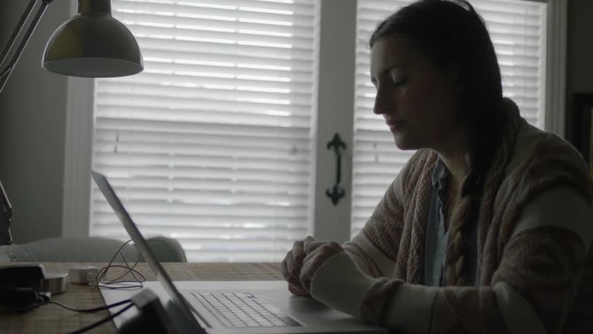 A young woman sits at a desk staring at her laptop screen