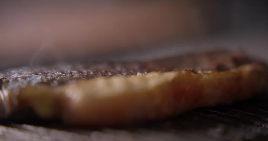 A piece of steak turned over while cooking on a open grill