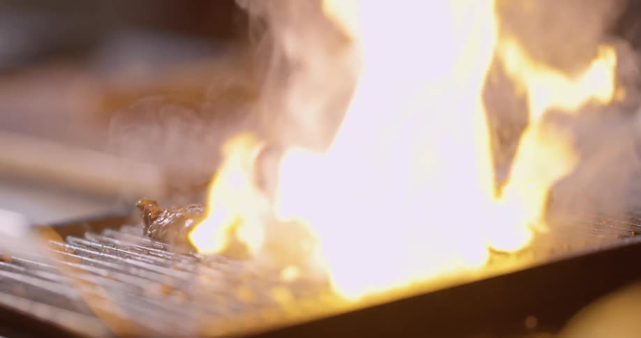 Smoke and flames come from a patty cooking on the grill