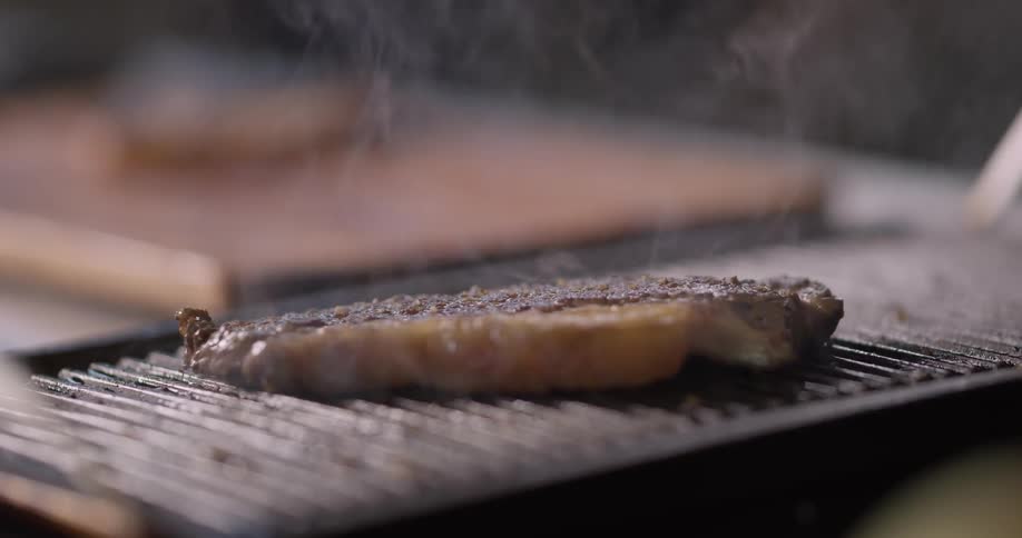 A piece of steak with a long strip of fat on its side can be seen cooking away on a small grill