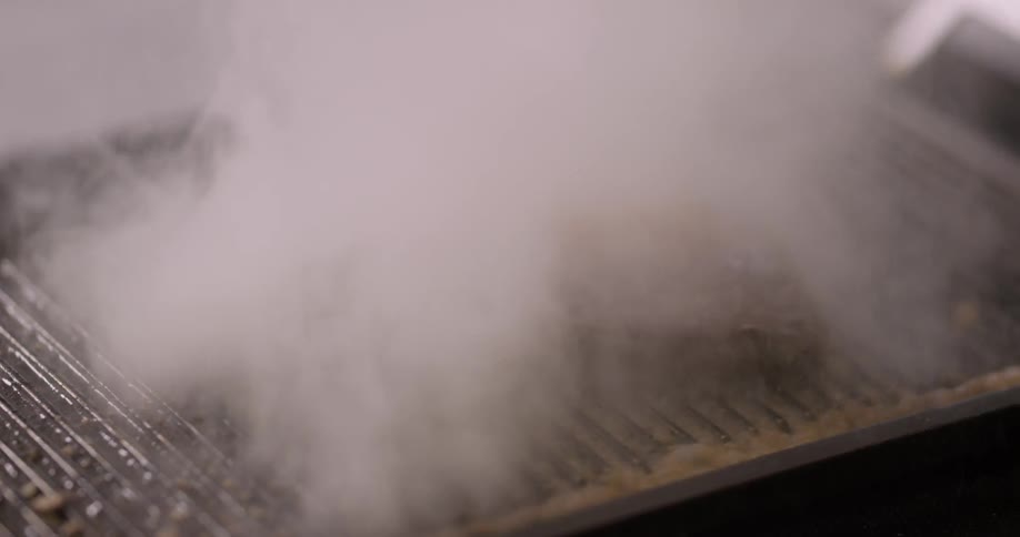 A person pouring oil on a steak on a skillet and lighting it on fire