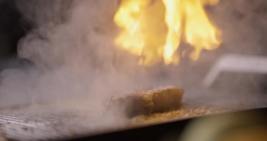 Someone is pouring alcohol over a grilling meat and alcohol goes ablaze