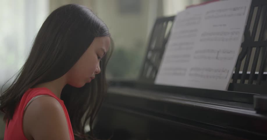 A young asian female is seen sitting at a piano and is concentrating as she plays a song