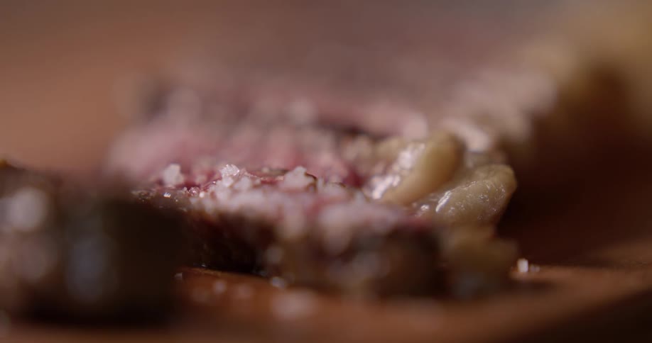 A person sprinkles salt onto red meat