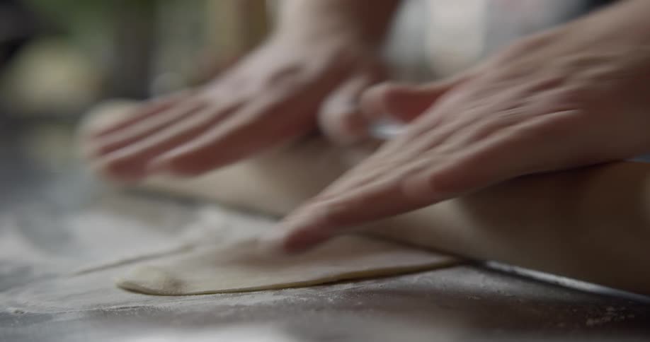 A person flattens dough on a table top