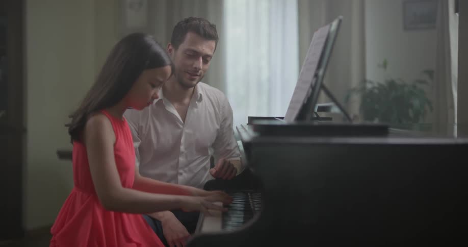 Girl plays on piano while teacher watches