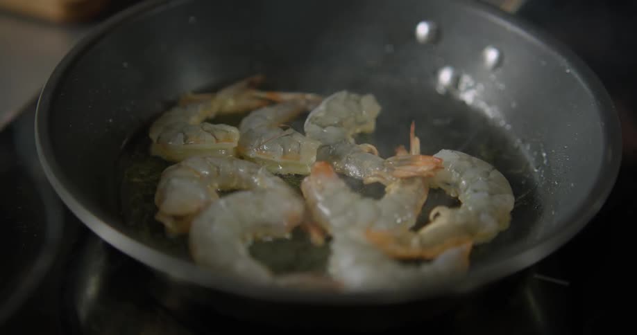 A person frying shrimp in a frying pan