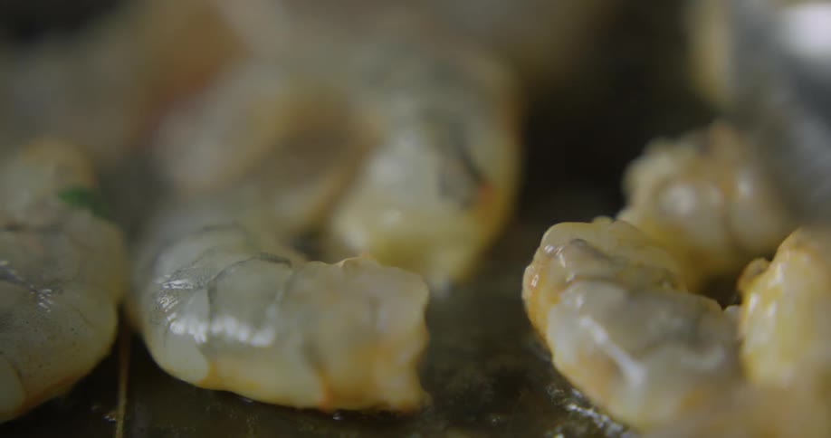 Shrimp is stirred with a spoon while it is cooking on a hot skillet
