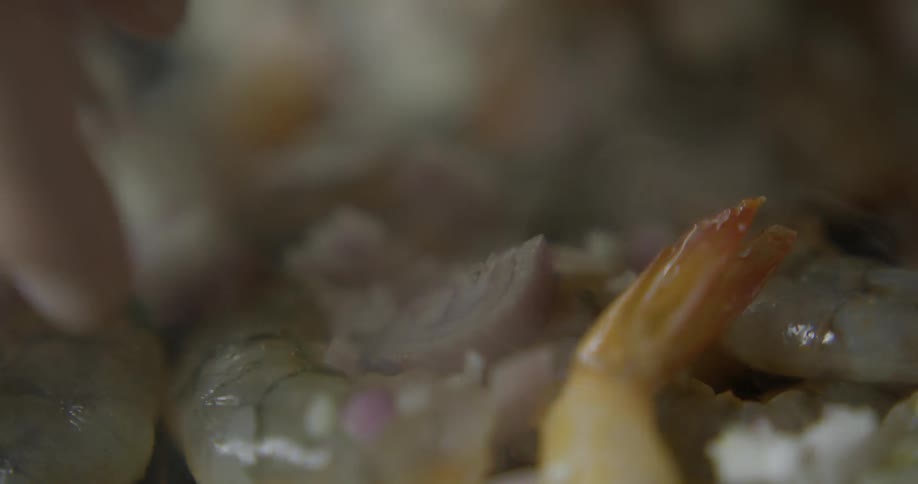 A hand sprinkling onions on shrimp as its cooking