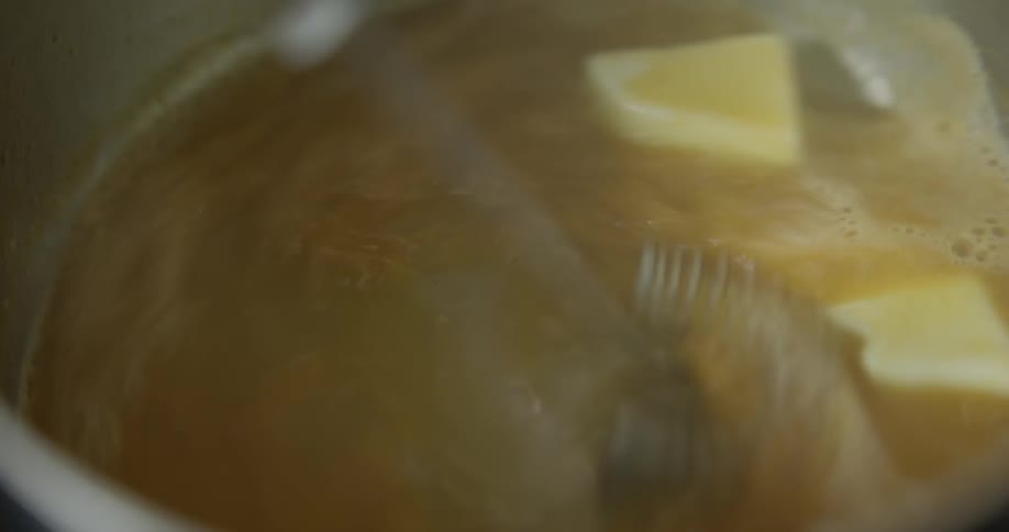 A hand stirring melted butter in a pot