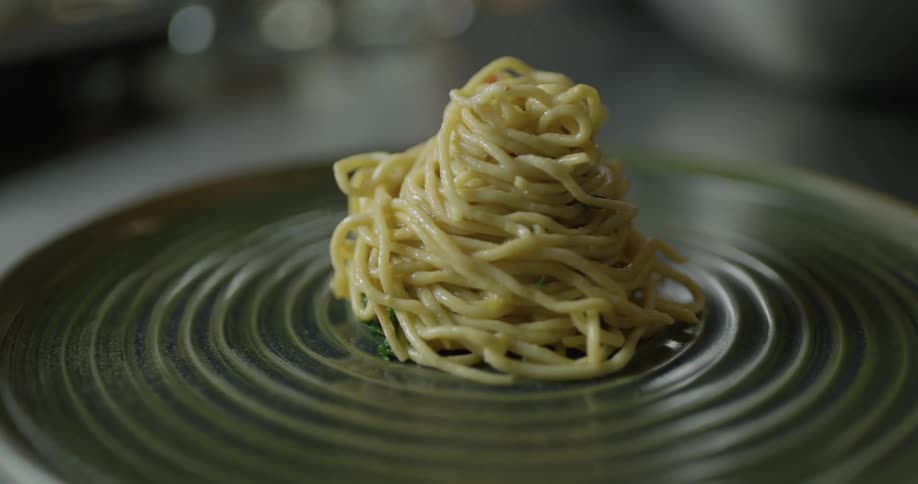 A person makes a pile of noodles on a plate and puts shrimp on them