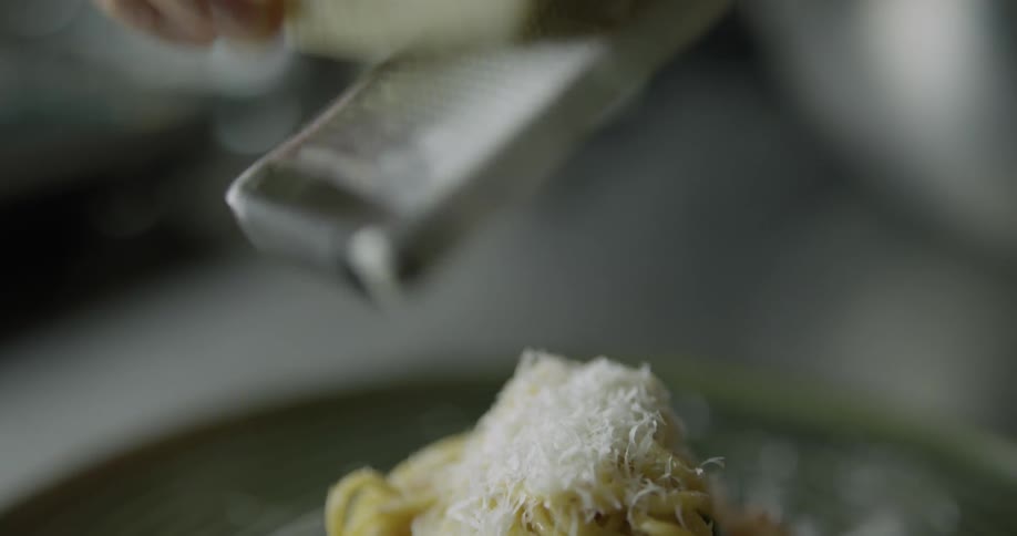 A person is grating cheese on noodles