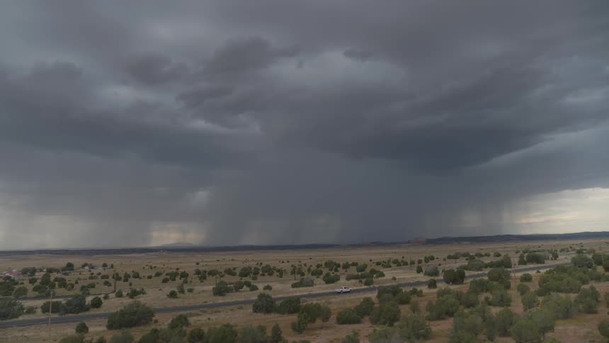 A white vehicle driving down the road with the sky and clouds in the background