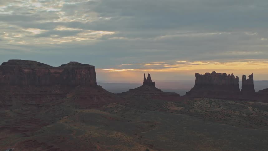 The camera looks across a desert landscape with sandstone towers