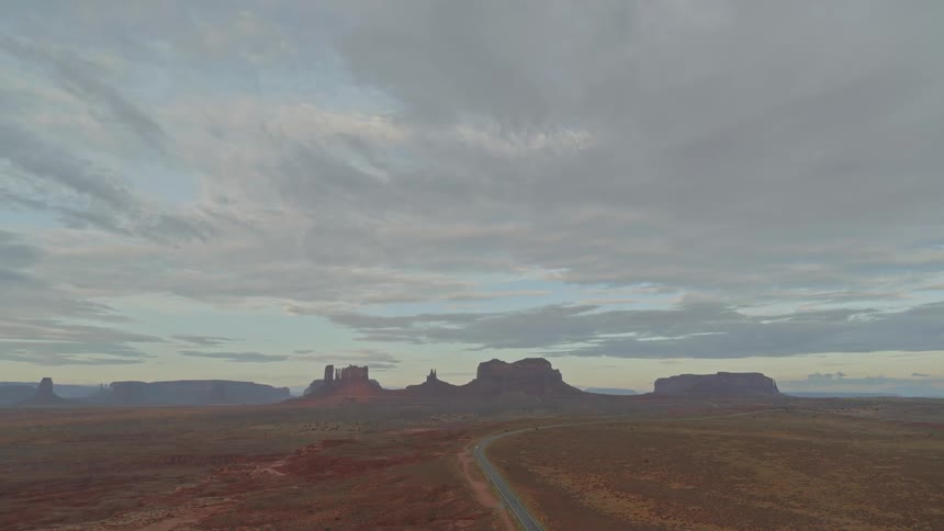 Wispy clouds over red rock and sand with a 2 lane highway running through