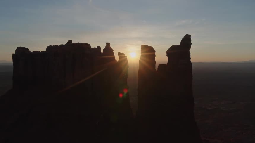 The sun is low in the cast which cast a beautiful palette of colors through the desert sky while the sun also peeks through a jagged rock formation in Utah
