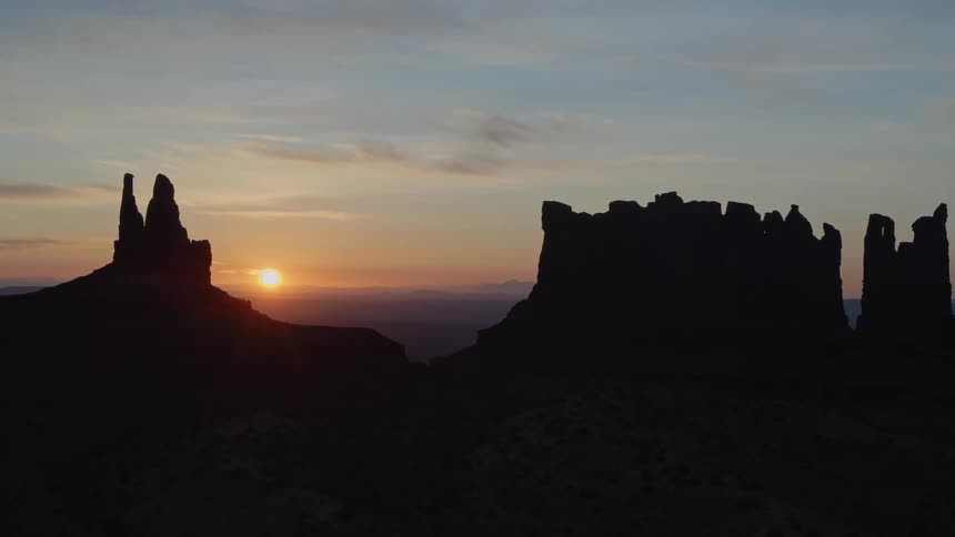 The sun sets behind a desert landscape with large stone cliffs