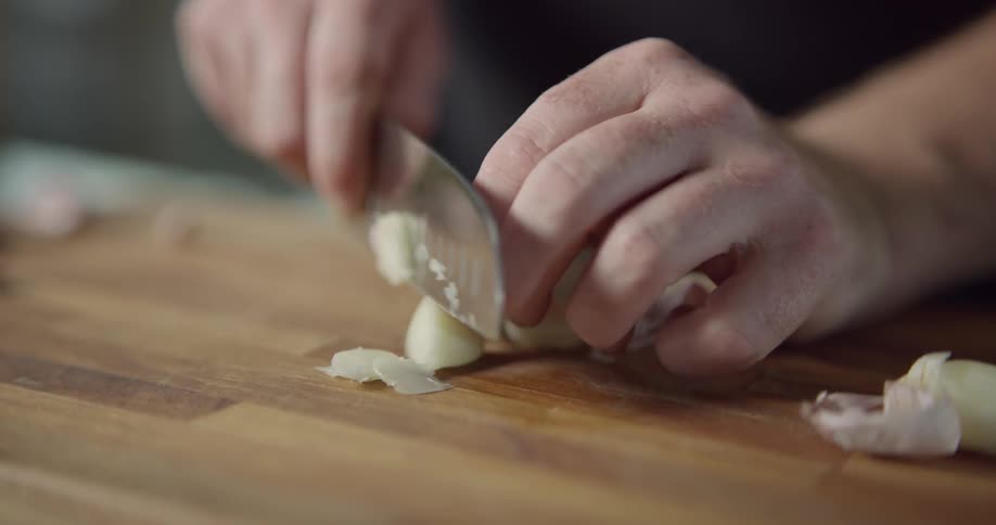 Man chops shallot on cutting board in the kitchen during daylight