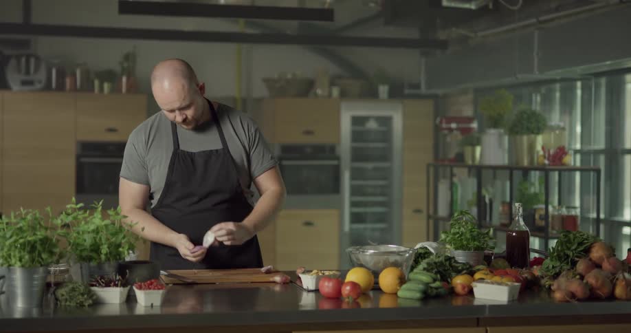 Cook wearing black apron chops onion in the kitchen during daylight