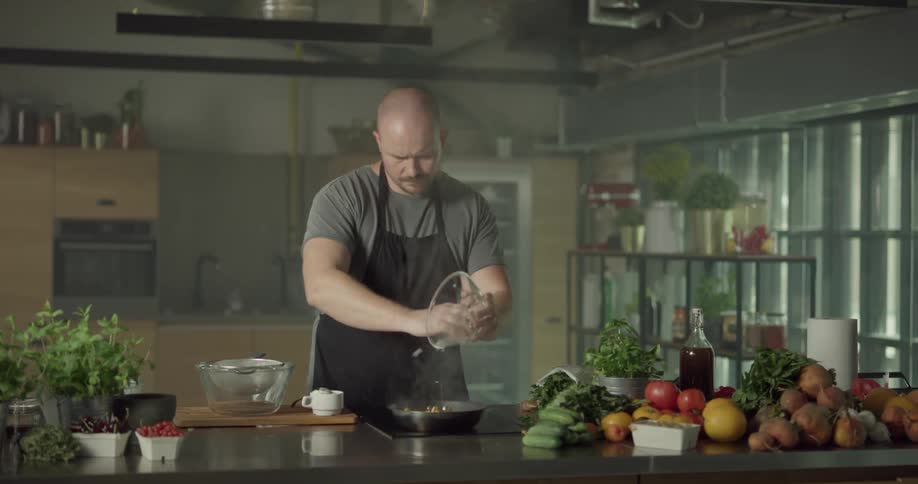 Man wearing an apron sauteing chicken and onions together in a pan on the stove