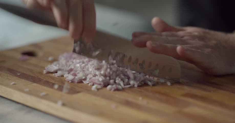 Man chops onion fast on cutting board with knife in the kitchen during daytime