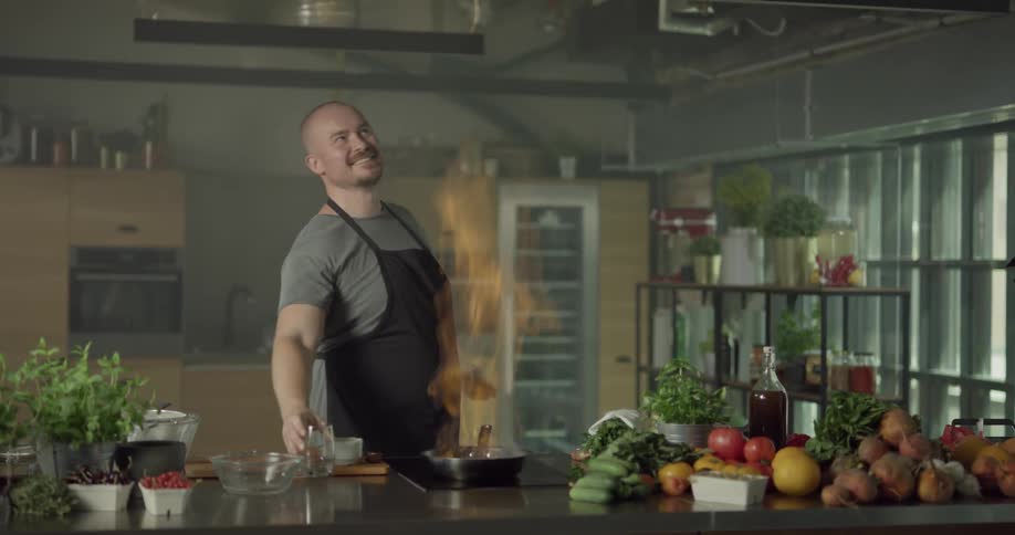 A man picks up a glass of water and pours it in a pan and gets flames