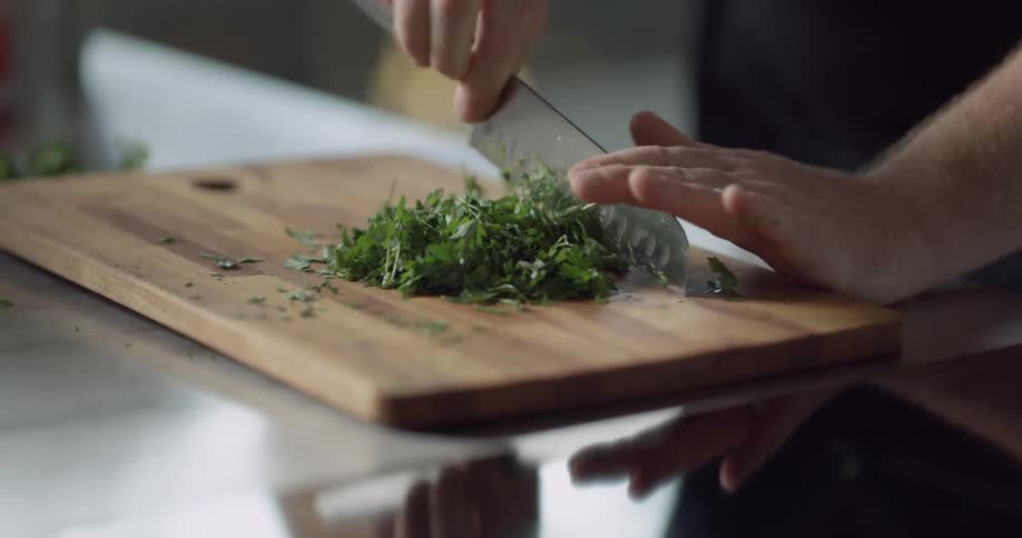 A cook cuts herbs with a chef's knife