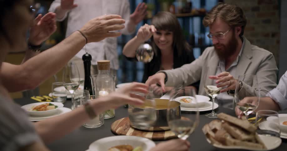 A woman ladles soup into a bowl as a group of friends has dinner together