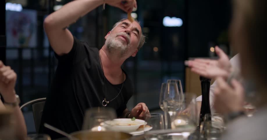 Friends laugh as a man dips a shrimp into his mouth from above