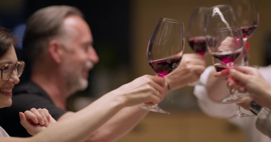 A chef and other people sitting around a table toasting with red wine